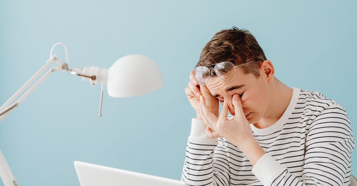 Young man at a laptop pinching the bridge of his nose while trying to concentrate