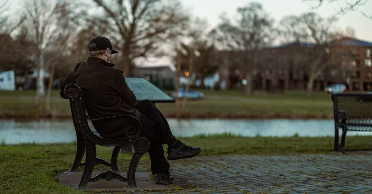 Man resting on a park bench by water, pacing a short walk while recovering from flu