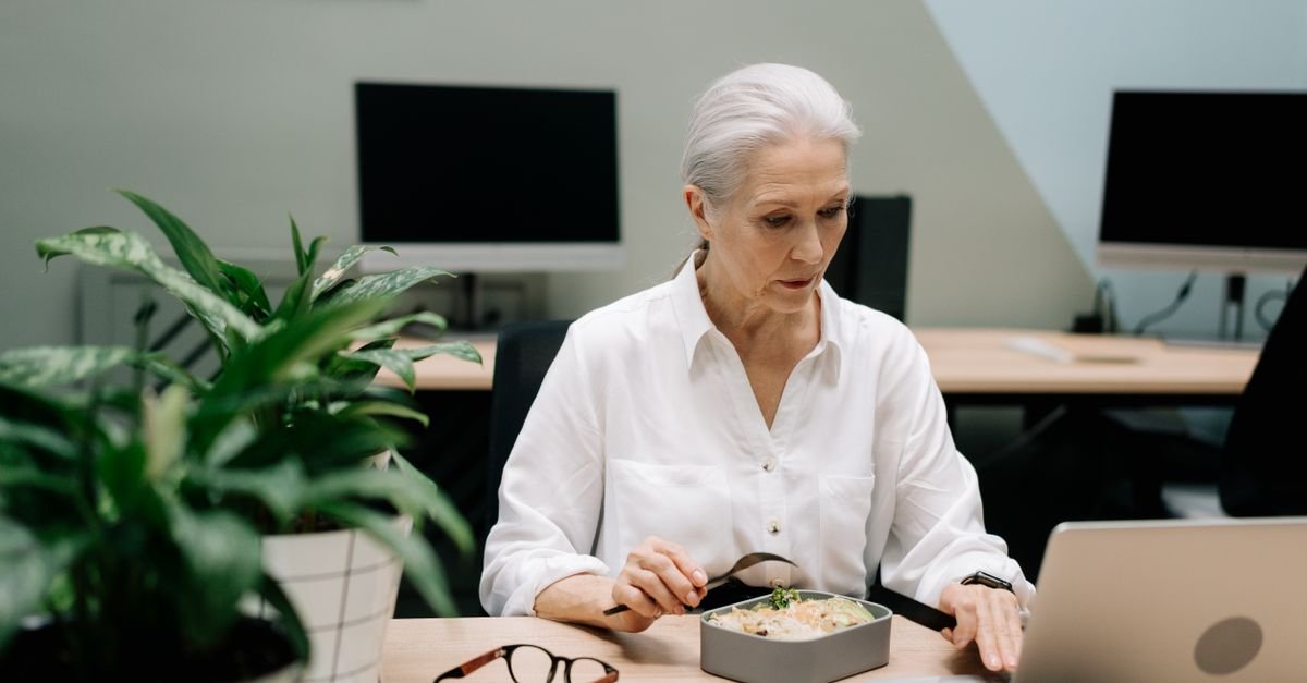 Older woman eating lunch at her office desk, food after a long gap when brain fog hits