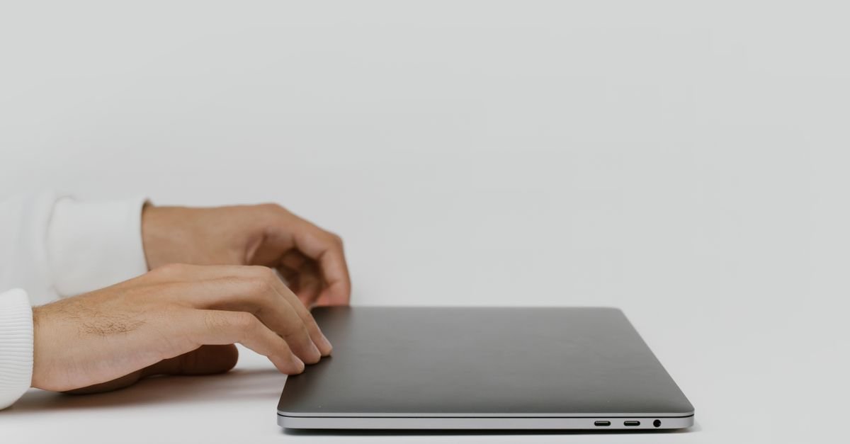 Hands closing a laptop lid on a plain desk, stepping away from the screen with brain fog