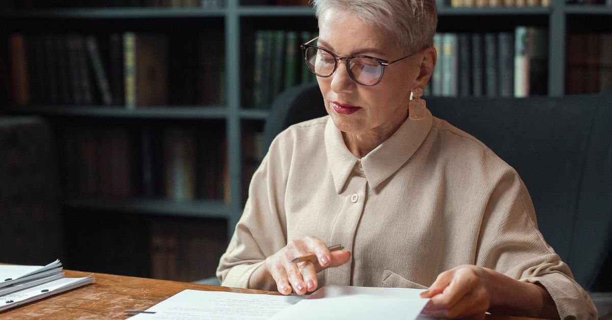 Older woman in glasses reading printed research papers at a desk, reading the creatine brain fog trials