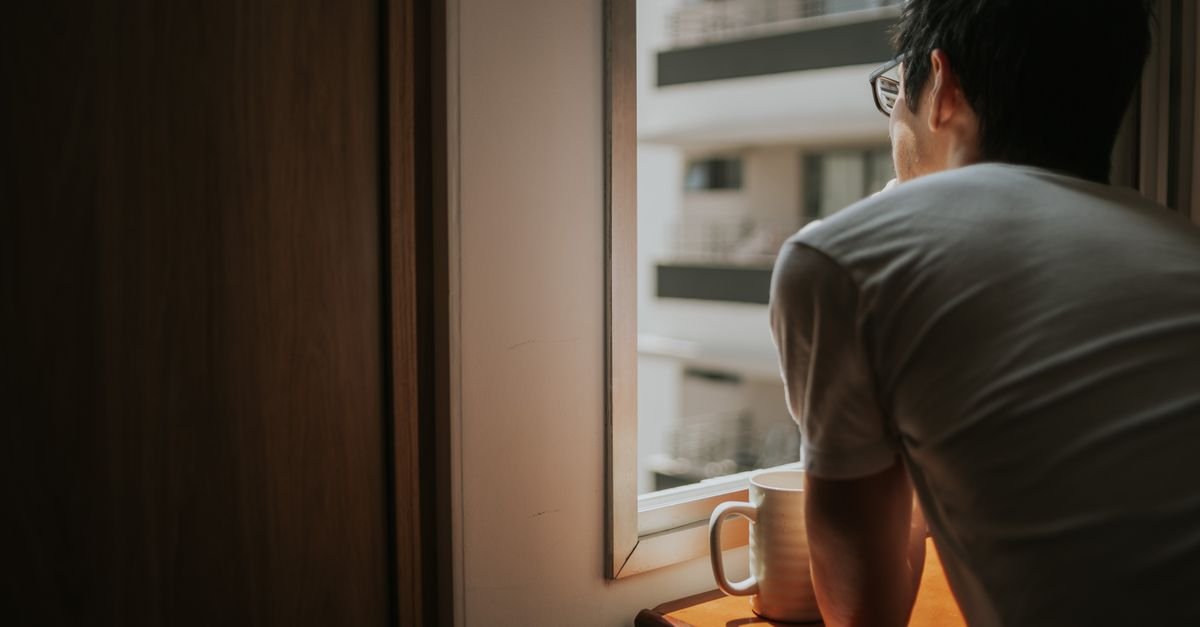 Man holding a mug looking out a window at dusk, living with persistent brain fog