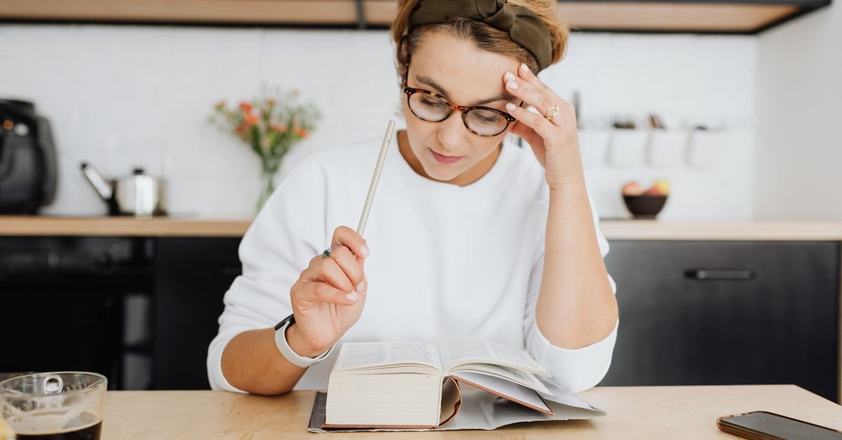 Woman with a pencil and an open notebook at a kitchen table, pausing to find the right word