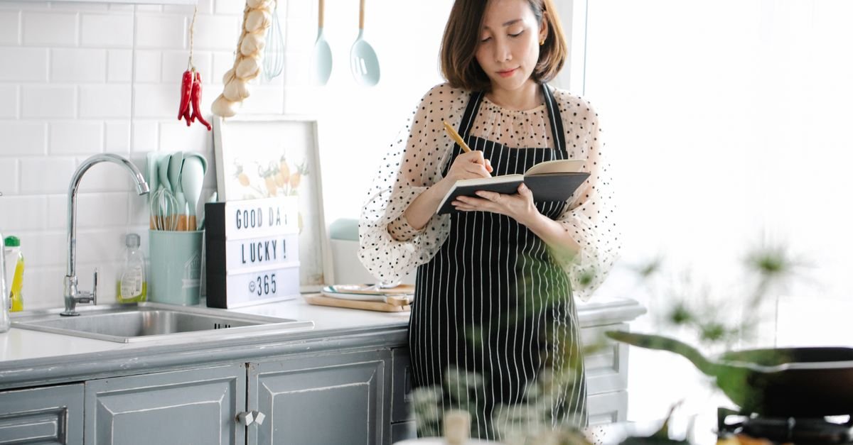 Woman in a bright kitchen writing a list in a notebook to work around menopause forgetfulness
