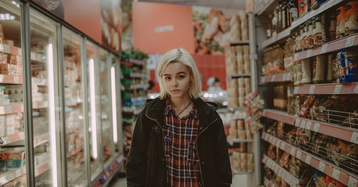 Woman standing still in a supermarket aisle, the blank pause of mental tiredness