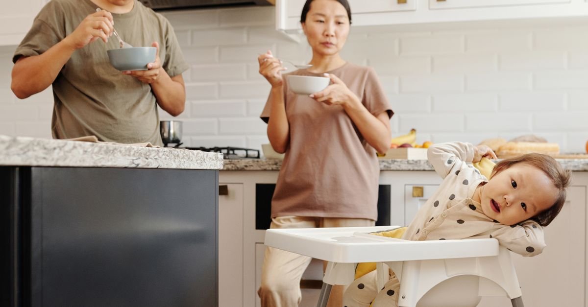 Mother eating standing up in the kitchen while her baby sits in a high chair