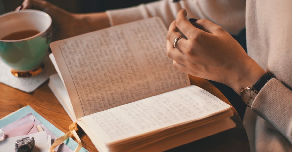Hands writing notes in a journal beside a mug, tracking postpartum brain fog before an appointment